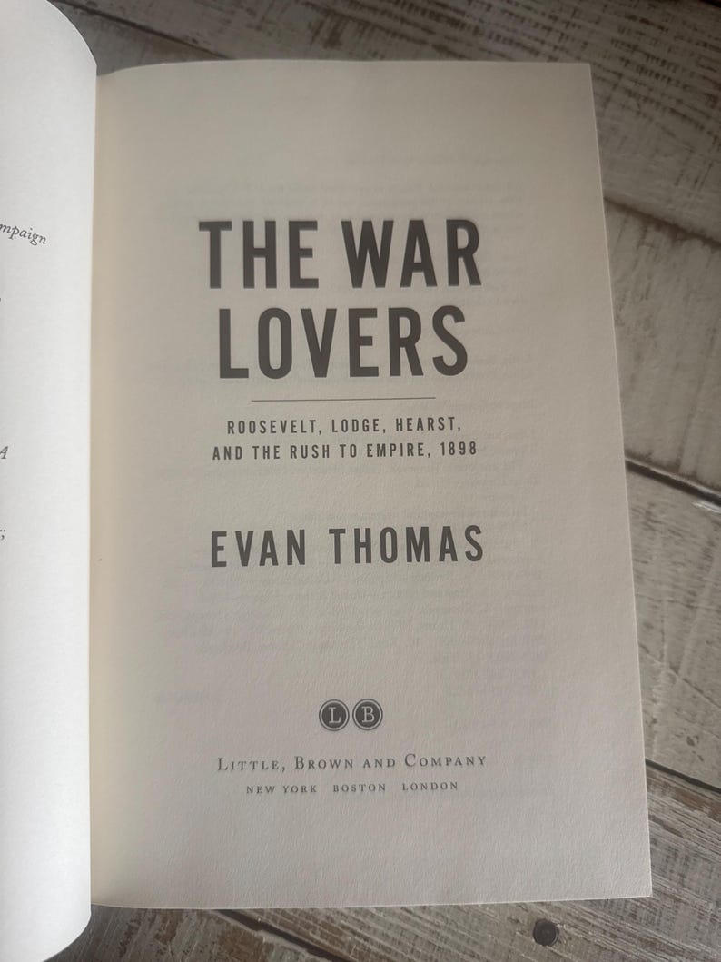 May include: Open book with the title "THE WAR LOVERS" in large, dark gray letters. Below, smaller text reads "ROOSEVELT, LODGE, HEARST, AND THE RUSH TO EMPIRE, 1898." The author's name, EVAN THOMAS, is also visible. The book is published by Little, Brown and Company.