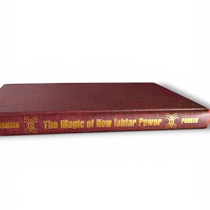 Puede incluir: Un libro de tapa dura de color granate titulado "The Magic of New Ishtar Power" con letras doradas. El lomo del libro presenta el nombre del autor y el nombre de la editorial. El libro est&aacute; sobre un fondo blanco.