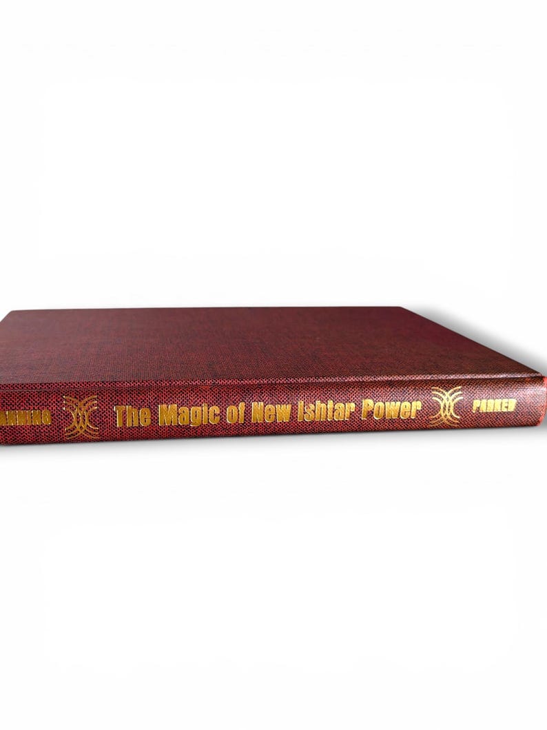 Puede incluir: Un libro de tapa dura de color granate titulado "The Magic of New Ishtar Power" con letras doradas. El lomo del libro presenta el nombre del autor y el nombre de la editorial. El libro est&aacute; sobre un fondo blanco.