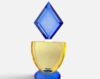 May include: A decorative glass object featuring a blue diamond-shaped topper, a central yellow semi-circular body with a textured surface, and a rounded blue base. The piece is constructed from translucent colored glass segments stacked vertically.