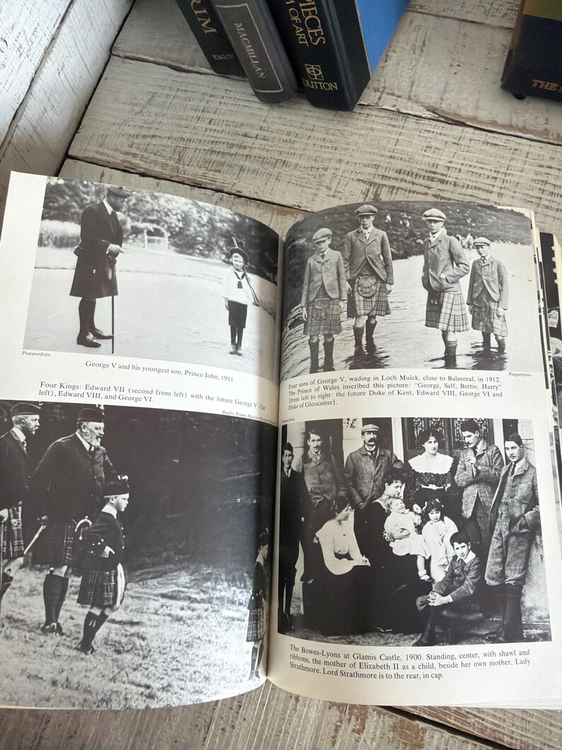 May include: An open book featuring historical black and white photographs. The images depict George V and his son, Prince John, and other members of the royal family in Scotland, wearing kilts and formal clothing.