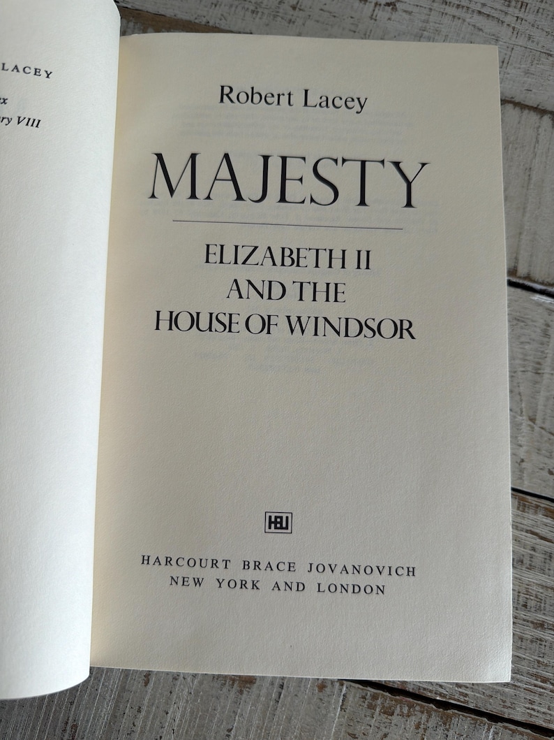 May include: An open book titled "MAJESTY" by Robert Lacey. The subtitle reads "ELIZABETH II AND THE HOUSE OF WINDSOR." Published by Harcourt Brace Jovanovich, with locations in New York and London. The book's pages are off-white.