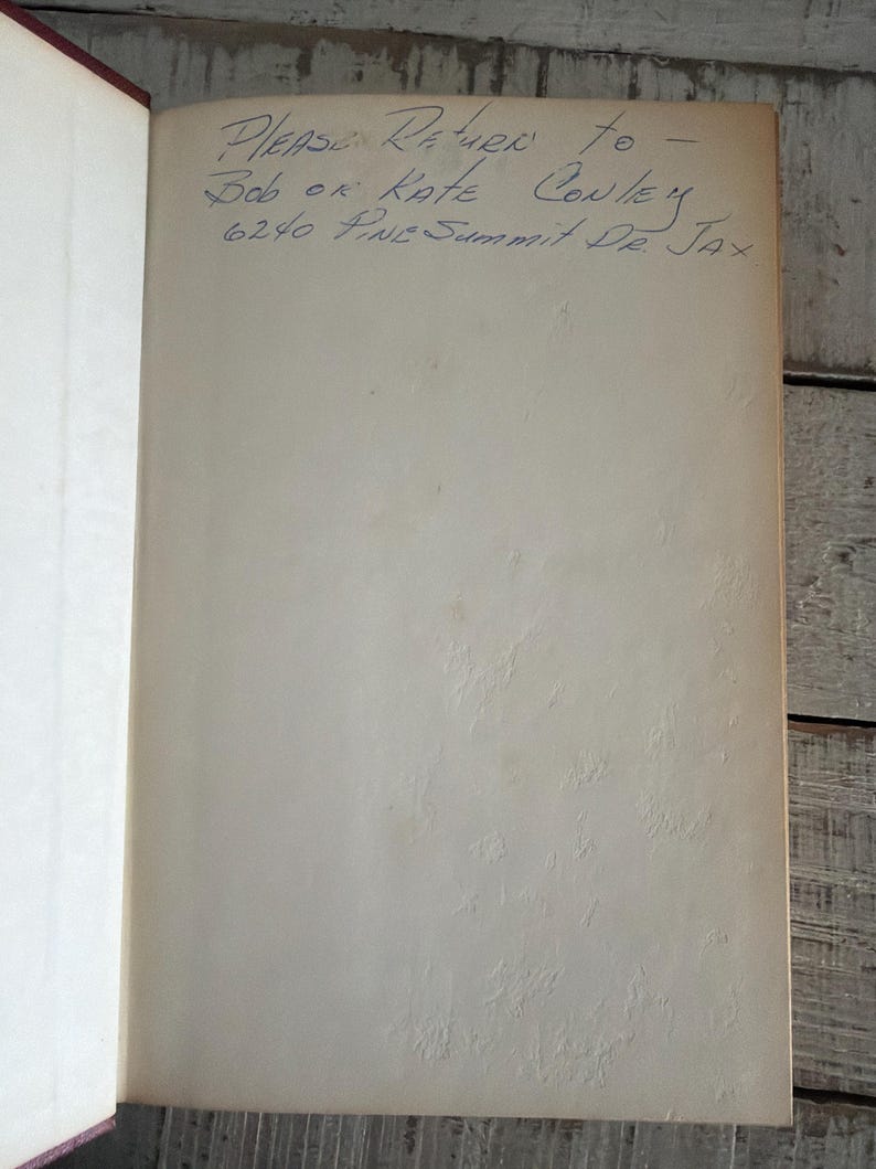Puede incluir: Libro abierto con texto manuscrito en tinta azul. El texto dice "Please Return to - Bob or Kate Conley 6240 Pine Summit Dr. Jax". Las p&aacute;ginas son blanquecinas con una apariencia texturizada.