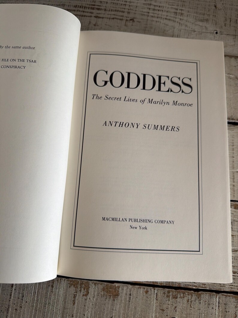 May include: An open book displaying the title "GODDESS" in bold black font. The subtitle reads "The Secret Lives of Marilyn Monroe" by Anthony Summers. The Macmillan Publishing Company is also listed.