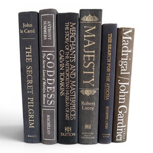 May include: A selection of seven hardback books with spines in shades of grey and brown. Titles include "The Secret Pilgrim," "Goddess," and "Majesty," with gold lettering. The books are arranged vertically against a white backdrop.