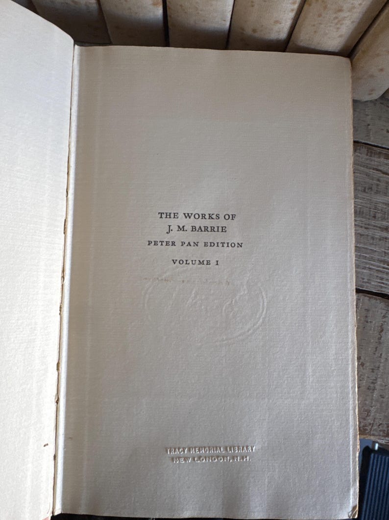 Puede incluir: Libro abierto que muestra la p&aacute;gina de t&iacute;tulo de "The Works of J.M. Barrie, Peter Pan Edition, Volume 1". El texto en negro sobre una p&aacute;gina color crema. Tambi&eacute;n aparece la inscripci&oacute;n "Tracy Memorial Library, New London, H.H.".