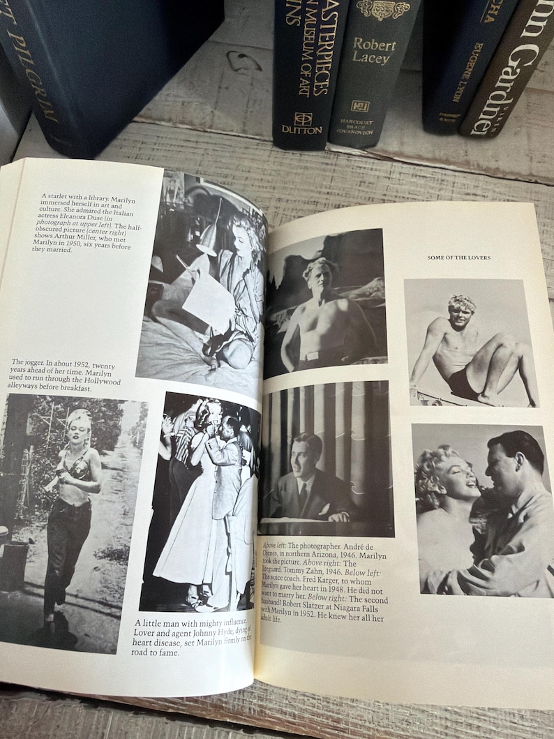 May include: An open book featuring black and white photographs of Marilyn Monroe. The book displays various images, including portraits and candid shots. Several books are visible in the background.