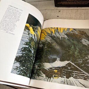May include: An open book displaying a print titled CHILI NIGHT 1977 by Bev Doolittle. The illustration features a snow-covered cabin at night with dark green pine trees, a bright yellow sky, and two horses standing near the cabin entrance.