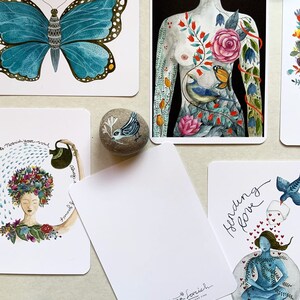 May include: Set of five illustrated cards featuring a blue butterfly, a woman's torso with floral and bird imagery, a woman with a flower crown, a blank card with the artist's name and website, and a woman meditating with a bird and hearts. The cards are printed on white cardstock and have a matte finish.