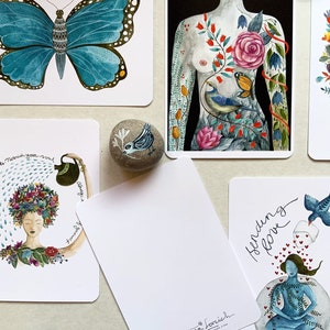 May include: Set of five illustrated cards featuring a blue butterfly, a woman's torso with floral and bird imagery, a woman with a flower crown, a blank card with the artist's name and website, and a woman sitting in a lotus position with a bird and hearts.