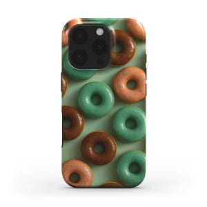 May include: A phone case with a repeating pattern of donuts in shades of brown, orange, and green. The donuts are set against a light green background. The case has a glossy finish and a camera cutout.