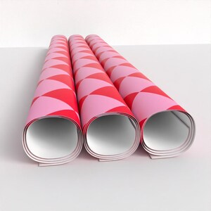 May include: Three rolls of pink and red patterned wrapping paper. The paper is rolled up and the ends are visible.