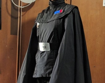 May include: A black officer's uniform with a black cape and a silver belt buckle. The uniform has a blue and red patch on the left shoulder.