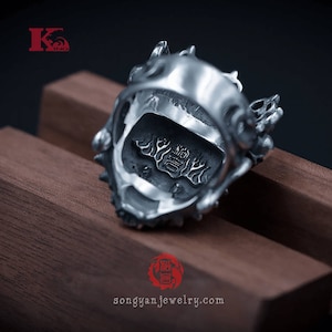 K&ouml;nnte beinhalten: Ein silberner Ring mit einem detaillierten Drachen-Design. Der Ring liegt auf einer Holzoberfl&auml;che und die Innenseite des Rings ist mit chinesischen Schriftzeichen gepr&auml;gt.
