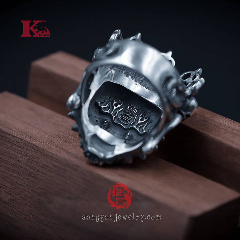 K&ouml;nnte beinhalten: Ein silberner Ring mit einem detaillierten Drachen-Design. Der Ring liegt auf einer Holzoberfl&auml;che und die Innenseite des Rings ist mit chinesischen Schriftzeichen gepr&auml;gt.