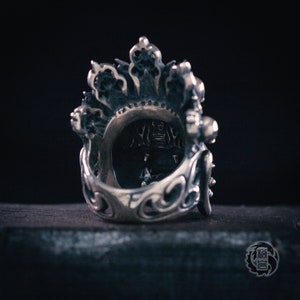 K&ouml;nnte beinhalten: Ein silberner Ring mit filigranen Details und einem kronenartigen Design. Der Ring ist aus Metall und hat ein detailliertes Design.