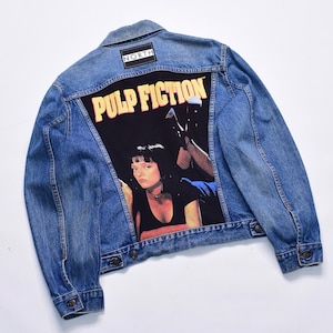 May include: A blue denim jacket featuring a graphic from the film "Pulp Fiction" on the back. The graphic includes the film's title in yellow and a portrait of a woman. The jacket has a "NORTH" patch.