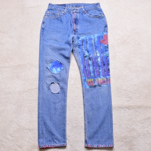 May include: Light blue denim jeans with distressed patches and a graphic design on the right leg. The graphic features the word "GUNS" in a vertical design with a red rose and the text "USE YOUR ILLUSION".