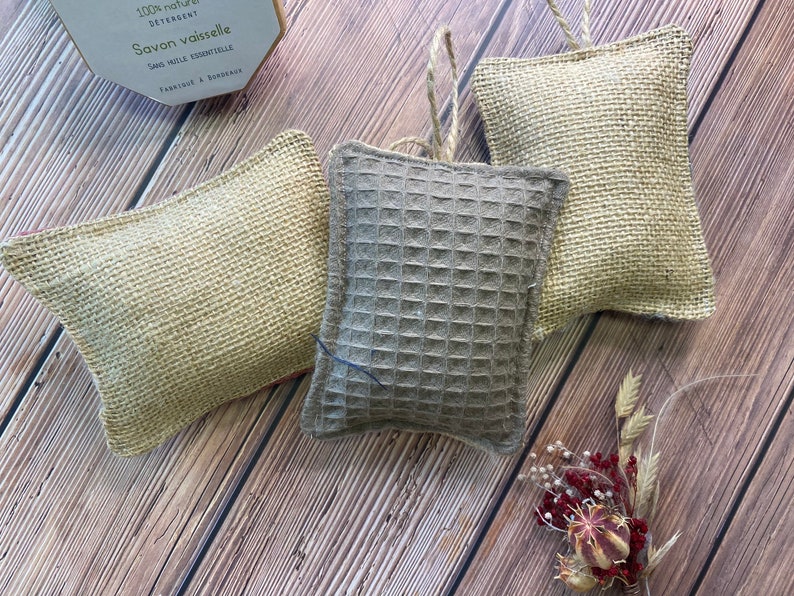May include: Three dishcloths, two are made of natural burlap and one is a gray waffle weave. The dishcloths are hanging from a string.