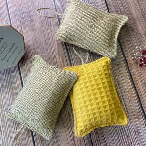 May include: Three natural dishcloths, two are made of burlap and one is a yellow waffle weave. The dishcloths are tied with twine and are on a wooden surface.