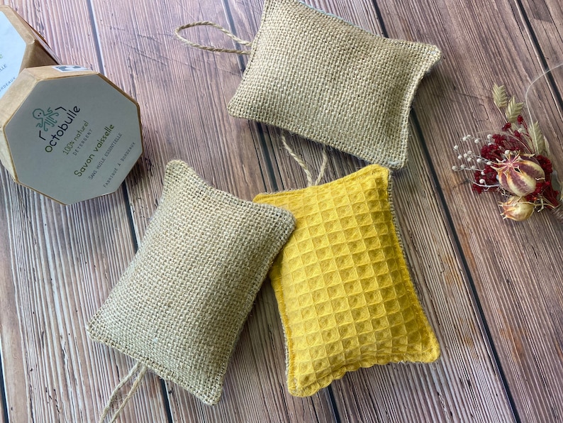 May include: Three natural dishcloths, two are made of burlap and one is a yellow waffle weave. The dishcloths are tied with twine and are on a wooden surface.