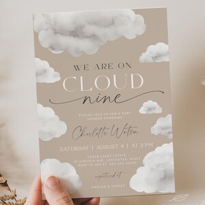 May include: A light brown baby shower invitation featuring a watercolour cloud design. The text reads "We are on cloud nine" and "Please join us for a baby shower honouring Charlotte Watson". The invitation also includes the date, time, and location of the shower, as well as the RSVP information. The text "registered at Amazon & Target" is also included.
