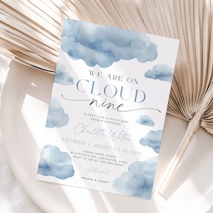 May include: A baby shower invitation with a blue watercolor cloud design. The text reads "We are on cloud nine" and includes the name "Charlotte Watson", the date "August 11", the time "3 PM", the location "Cedar Lakes Estate", and the address "45 Virginia Ave, Lancaster, 42683". The invitation also includes the RSVP information and the registry information.