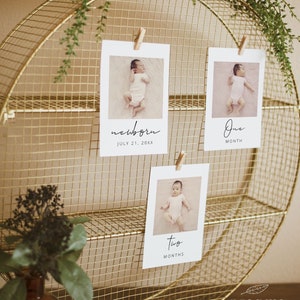 May include: A gold metal wire stand with three shelves. There are three white cards with photos of a baby on each card. The top card says 'newborn' and 'July 21, 20XX'. The middle card says 'one month'. The bottom card says 'two months'.