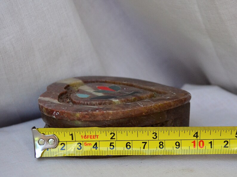 Puede incluir: Una caja de piedra de forma de coraz&oacute;n, de color marr&oacute;n, con piedras de colores incrustadas. La caja se est&aacute; midiendo con una cinta m&eacute;trica que indica 10 pulgadas.