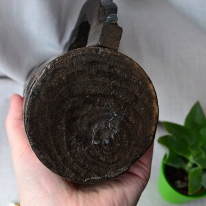 May include: The bottom of a dark brown wooden pitcher with a carved design. The pitcher is being held by a hand.