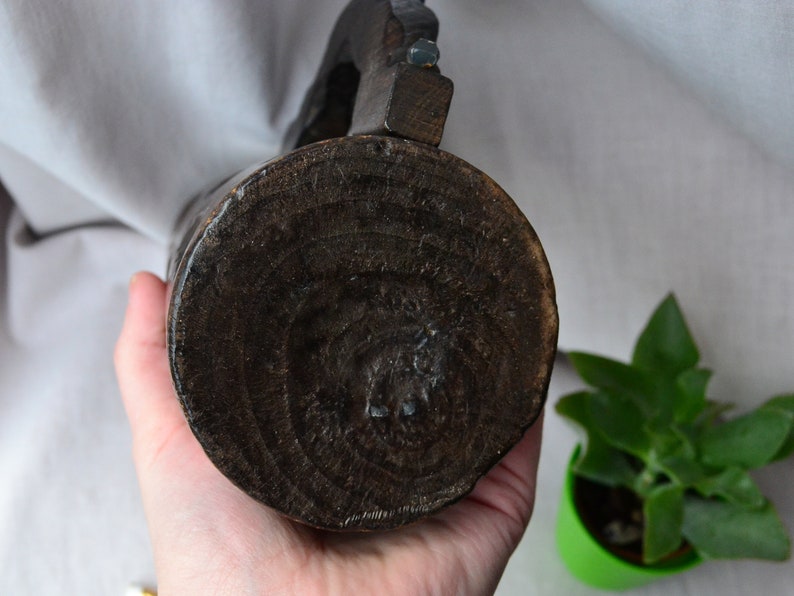 May include: The bottom of a dark brown wooden pitcher with a carved design. The pitcher is being held by a hand.