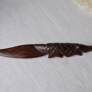 May include: A dark brown wooden letter opener shaped like an alligator with a textured back.
