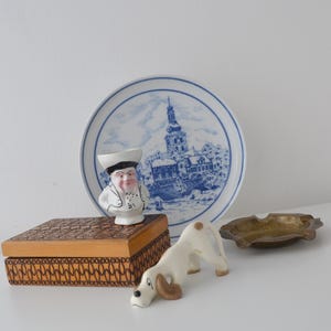 May include: A selection of vintage decorative items. Includes a blue and white plate with a town scene, a ceramic chef figurine, a wooden box, a ceramic dog figurine, and a small brass ashtray.