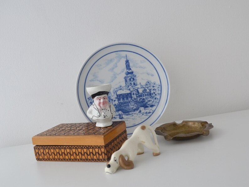 May include: A selection of vintage decorative items. Includes a blue and white plate with a town scene, a ceramic chef figurine, a wooden box, a ceramic dog figurine, and a small brass ashtray.