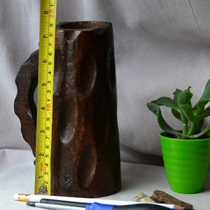 May include: A dark brown wooden mug with a carved handle. The mug is approximately 10 inches tall.