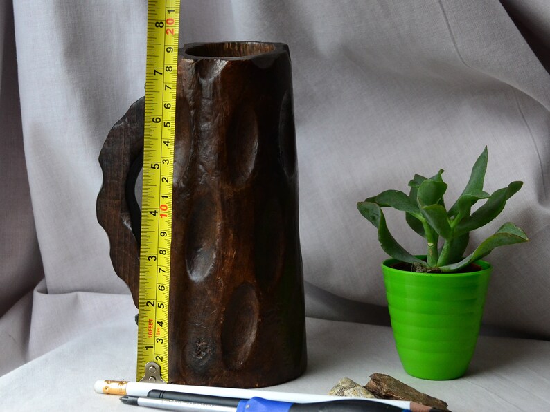 May include: A dark brown wooden mug with a carved handle. The mug is approximately 10 inches tall.