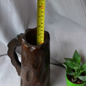 May include: A dark brown wooden beer stein with a carved handle and a textured surface. The stein is approximately 8 inches tall.