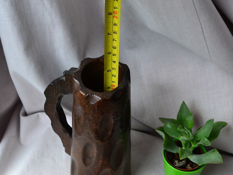 May include: A dark brown wooden beer stein with a carved handle and a textured surface. The stein is approximately 8 inches tall.