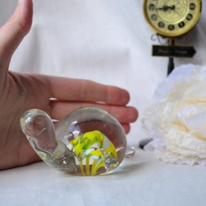 May include: A glass turtle figurine with a yellow and white swirl inside. The turtle is sitting on a white surface.