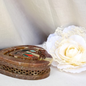 Puede incluir: Una caja de piedra de coraz&oacute;n marr&oacute;n con una incrustaci&oacute;n decorativa de piedras de colores. La caja tiene un dise&ntilde;o de celos&iacute;a alrededor del borde.