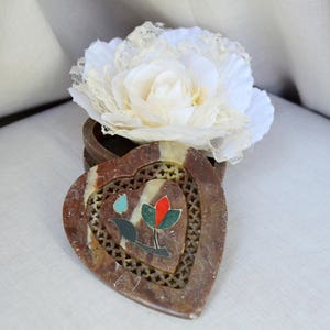 Puede incluir: Una caja de piedra de coraz&oacute;n, marr&oacute;n y blanca, con un dise&ntilde;o floral. La caja est&aacute; abierta y una flor de encaje blanco est&aacute; encima.