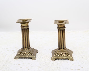 May include: A pair of gold metal candle holders with a fluted column design and ornate base.