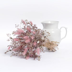 May include: A bouquet of dried pink bunny tail grass and white pussy willow branches tied with twine, next to a white ceramic pitcher.