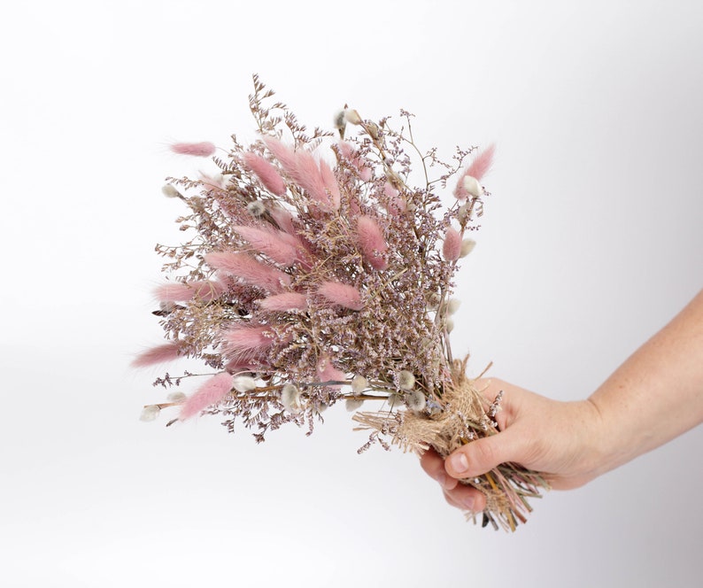 May include: A bouquet of dried pink and white flowers, tied with twine. The bouquet is held in a hand.