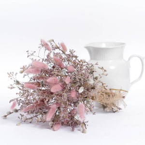 May include: A bouquet of dried pink bunny tail grass and dried willow branches arranged in a white ceramic pitcher.