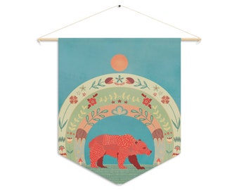 Può includere: Un arazzo da parete con un orso rosso che cammina attraverso un arco floreale colorato. Lo sfondo è di colore azzurro chiaro con un sole giallo.