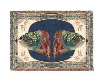 May include: A rectangular woven throw blanket featuring a mirrored design of two fish heads facing outward. The central dark blue oval is surrounded by a cream-colored border with decorative patterns and a fringed edge in shades of blue and gold.