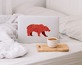 Può includere: Un adesivo di un orso rosso con motivo su un computer portatile bianco. Il computer portatile è su un letto bianco con una coperta bianca e un vassoio di legno marrone con una tazza di caffè bianca.