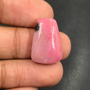 Puede incluir: Un cabujón de piedra preciosa rosa y blanca con inclusiones negras. La piedra preciosa está tallada en forma de lágrima y tiene una superficie lisa y pulida.
