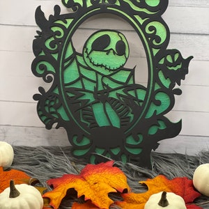 Pode incluir: Um recorte de madeira preto e verde de Jack Skellington de O Estranho Mundo de Jack, emoldurado em um design ornamentado. O recorte está sobre um fundo de madeira branca.